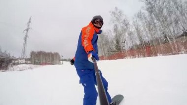 Bir snowboardcu orman boyunca geniş bir yoldan dağdan iner. Selfie çubuğundan ön görünüm