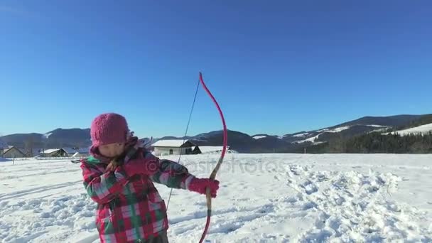 Chica jugando con arco y flecha en la nieve — Vídeos de Stock