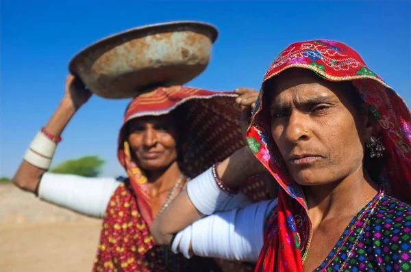 Rabari tribeswomen stanąć w polu sobie sarees i naramiennego bransoletki. Równoważy jedno wiadro na głowę. Rabari są społeczności indyjskiej w stanie Gujarat. — Zdjęcie stockowe