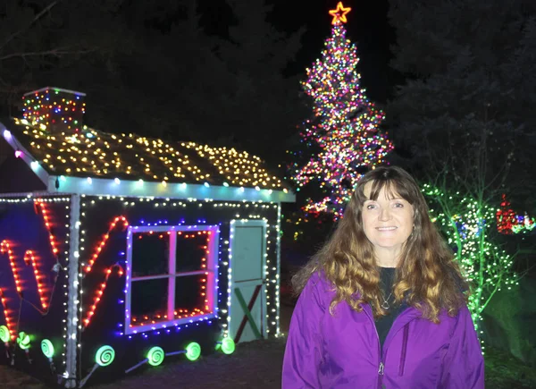 Una hermosa mujer sonriente con luces navideñas detrás — Foto de Stock