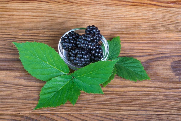 Küçük bir kapta olgun böğürtlen. Yeşil böğürtlen yaprakları. Rubus