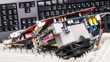 Parçalanmış donanım yedek parçaları ve klavyeler. E-atık ayıklama. Elektronik bileşenleri olan bilgisayar grafikleri ve anakart, kadın konnektörleri, anılar ve plastik vantilatörlü alüminyum ısı lavabosu.