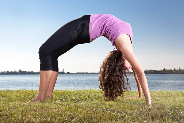 Beautiful young woman doing yoga exercise on green grass next to the lake. Yoga concept