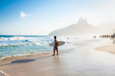 Rio De Janeiro, Brezilya - Nisan 24, 2015: Brezilyalı sörfçü Nisan'da Ipanema Beach Two Brothers Dağı doğru sörf tahtası ile yürüyüş 24, 2015, Rio de Janeiro. Brezilya.