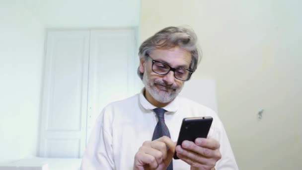 Ώριμος Άνδρας Ψάχνει Στο Smartphone Στο Γραφείο Του — Αρχείο Βίντεο