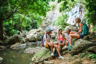 Orman nehir önünde konuşurken kayaların üzerinde oturan turist