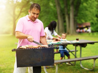 Baba barbekü partisinde aile için sosisli ve sucuk pişiriyor.