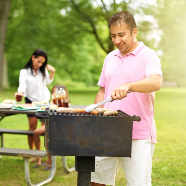 family barbecue - dad grilling with wife and daughter