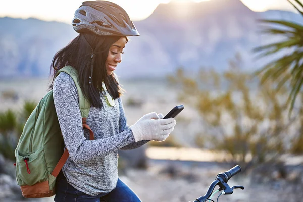 fit african american woman with bike stopping to use smartphone at red rock canyon park