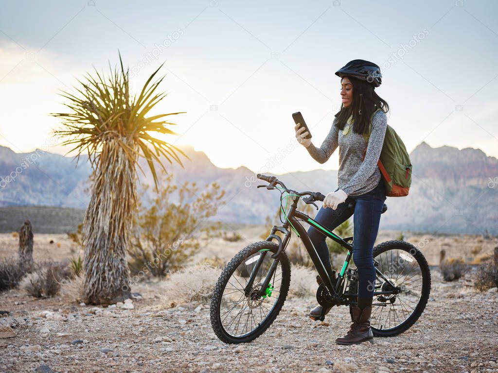 fit african american woman with bike stopping to use smartphone at red rock canyon park