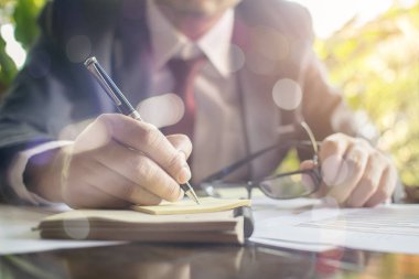 İş adamı kontrolü ciddi bir şekilde mali raporları analiz eder ve ofis finans yöneticilerinin iş ve finans konularındaki görevlerini ahşap masaya yazar.