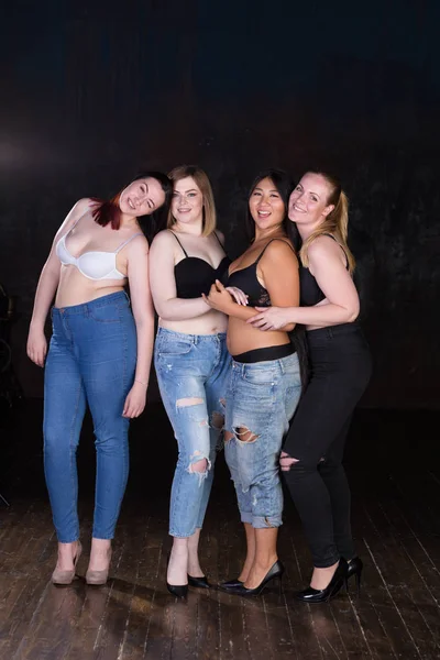 Quatro jovens mulheres meio vestidas bonitas em um fundo escuro se divertindo, rindo, sorrindo, brincando . — Fotografia de Stock