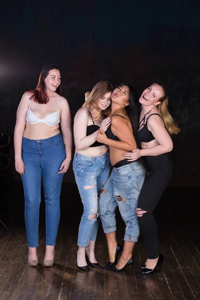 Quatro jovens mulheres meio vestidas bonitas em um fundo escuro se divertindo, rindo, sorrindo, brincando . — Fotografia de Stock