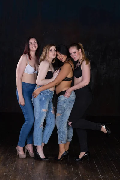 Quatro jovens mulheres meio vestidas bonitas em um fundo escuro se divertindo, rindo, sorrindo, brincando . — Fotografia de Stock
