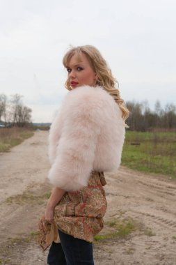 Genç sarışın kadın bej elbise ve kırsal yolda kısa pembe kürk manto