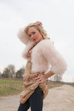 Genç sarışın kadın bej elbise ve kırsal yolda kısa pembe kürk manto