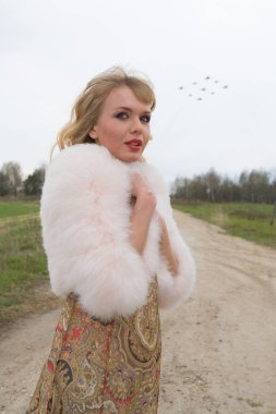 Genç sarışın kadın bej elbise ve kırsal yolda kısa pembe kürk manto