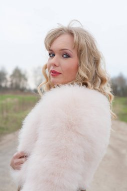 Genç sarışın kadın bej elbise ve kırsal yolda kısa pembe kürk manto