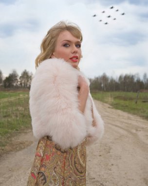 Genç sarışın kadın bej elbise ve kırsal yolda kısa pembe kürk manto