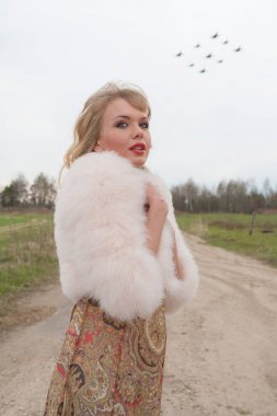 Genç sarışın kadın bej elbise ve kırsal yolda kısa pembe kürk manto
