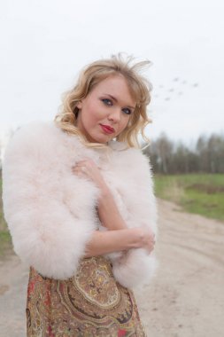 Genç sarışın kadın bej elbise ve kırsal yolda kısa pembe kürk manto
