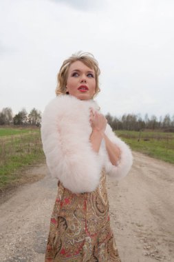 Genç sarışın kadın bej elbise ve kırsal yolda kısa pembe kürk manto