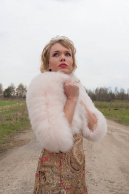 Genç sarışın kadın bej elbise ve kırsal yolda kısa pembe kürk manto