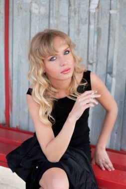 Güzel kadın modeli muhteşem klasik ceket ve kırsal yolda bir otobüs istasyonunda sigara oldukça siyah elbise