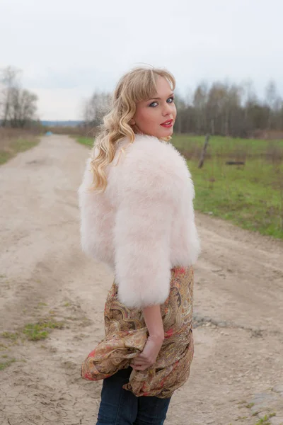 Genç sarışın kadın bej elbise ve kırsal yolda kısa pembe kürk manto