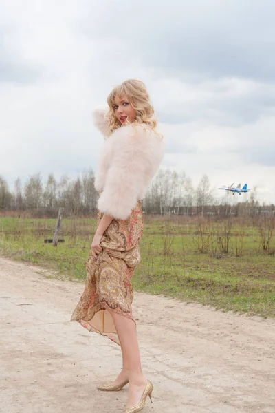 Genç sarışın kadın bej elbise ve kırsal yolda kısa pembe kürk manto