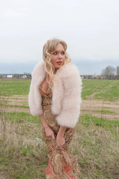 Genç sarışın kadın bej elbise ve kırsal yolda kısa pembe kürk manto