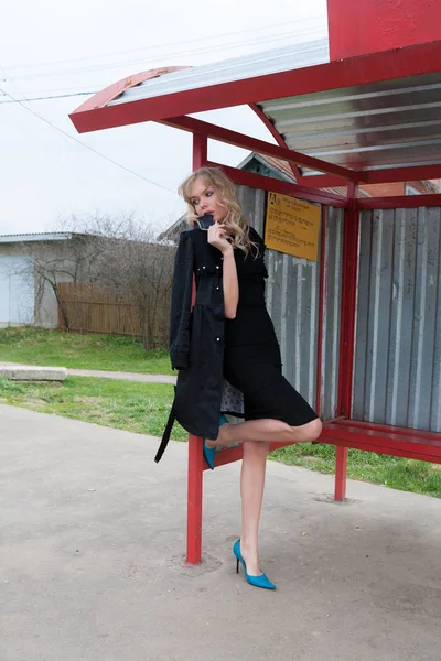 Güzel kadın modeli muhteşem klasik ceket ve kırsal yolda bir otobüs istasyonunda sigara oldukça siyah elbise