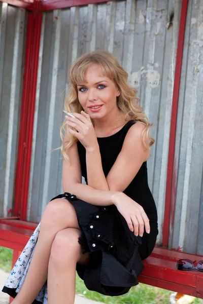 Güzel kadın modeli muhteşem klasik ceket ve kırsal yolda bir otobüs istasyonunda sigara oldukça siyah elbise