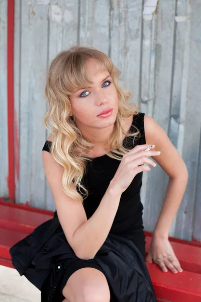 Güzel kadın modeli muhteşem klasik ceket ve kırsal yolda bir otobüs istasyonunda sigara oldukça siyah elbise