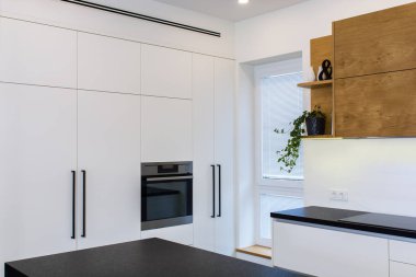 Modern Daire iç. Hafif iç ahşap desenli modern mutfak tasarımı. Kombine mutfak ve oturma odası. Avrupa mobilya, tasarım, teknoloji. Boyalı cephe. Siyah masa üstü.