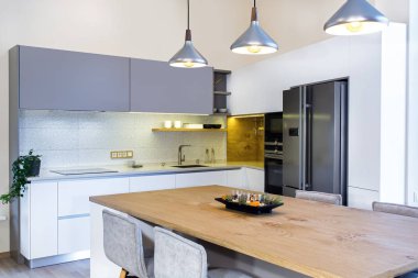 Hafif iç modern mutfak tasarımı. Odada mutfak adası. Mutfak ve oturma odası bir arada. Mutfak adasının üzerinde Yüzen Kolye Işığı. Güzel tasarım. Proje yönetimi. Meşe masa. Buzdolabı.