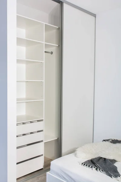 Modern home interior.Built-in wardrobe with sliding doors in the light interior of the bedroom. Small room. One of the doors of the built-in wardrobe is open. European furniture, design, technologies.