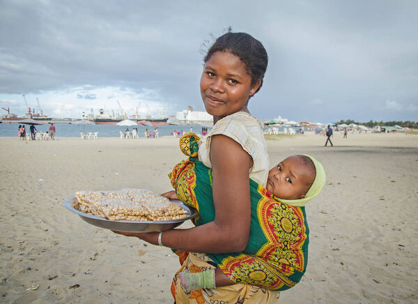 A malagasy girl with her baby is selling peanuts on the beach, Toamasina, Madagascar 11 Jul 2016