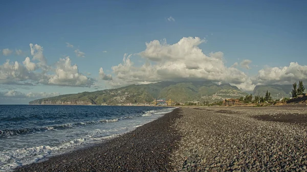Bir kayalık plaj ve bulutlar, Le Port, Reunion altında büyük yeşil tepeler