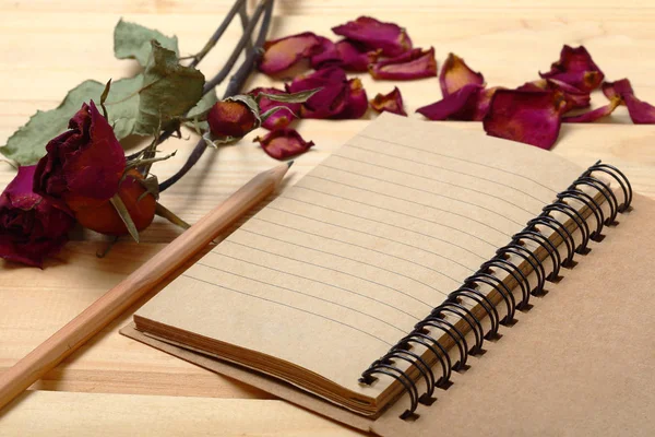 Empty notebook and dry roses with pencil on old wood — Stock Photo, Image