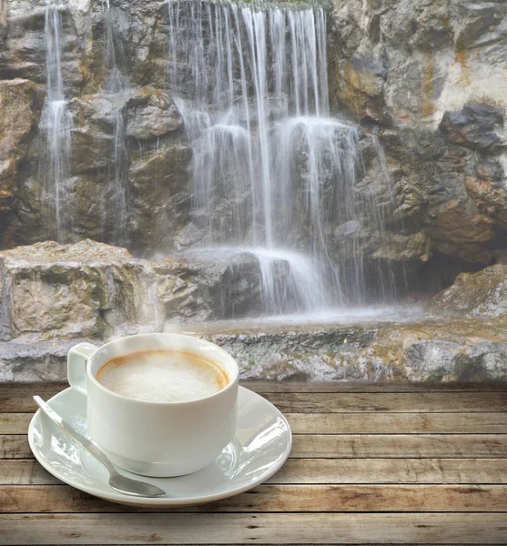 Кофе в белой чашке за деревянным столом с ложкой на водопаде — стоковое фото