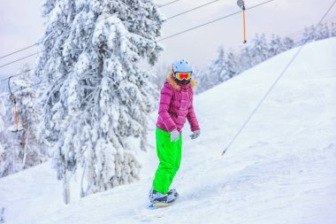 Karlı bir yamaçta bir kask ve gözlük takan bir snowboarder.