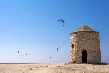 Yunanistan 'ın Lefkas adasındaki Agios Ioannis plajı. Renkli uçurtmalar uçurtma sörfçülerinden gökyüzüne kadar uzanıyor. Agios Ioannis eski yel değirmenlerinin evi..