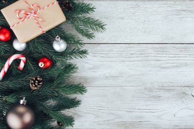 Noel konsepti. Kırmızı Noel mücevherleri, köknar ağacı dalları, yeşil hediye kutusu, şeker kamışı, beyaz tahta masadaki koniler. Yeni yıl, kış tatili, fotokopi alanı, üst manzara