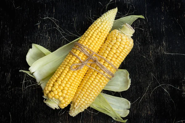 Two cobs of corn on a black wooden table — Stock Photo, Image