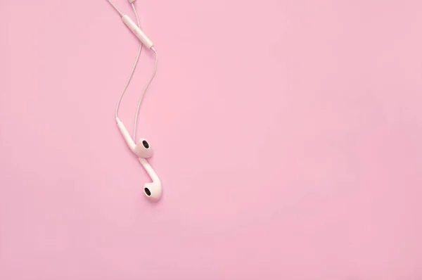 White earphones on pink background. Earphones for listening to music and sound on portable devices