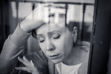genç güzel endişeli ve üzgün evde pencereden bakarak mutsuz Kafkas kadın depresif. değersiz ve ağrı hissediyor. portre. Depresyon ve kriz kavramı