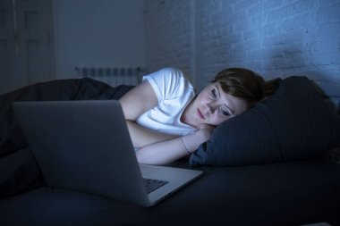 genç güzel, beyaz, kırmızı saçlı, Internet üstünde onu laptop yatak odasında yatakta gecenin karanlık odada sıkılmış, uykusuz ve yorgun çalışan kadın bağımlısı. Uykuya dalmak