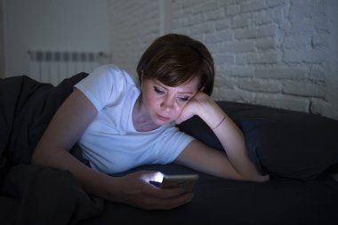 Genç çekici kadın uyanık geç gece karanlık bir yatak odasında yatakta yalan akıllı telefon kullanarak. Sohbet ve internet bağımlılığı, mobil istismar ve uykusuzluk kavramı iletileri göndermek için mobil kullanma