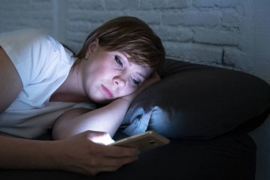Genç çekici kadın uyanık geç gece karanlık bir yatak odasında yatakta yalan akıllı telefon kullanarak. Sohbet ve internet bağımlılığı, mobil istismar ve uykusuzluk kavramı iletileri göndermek için mobil kullanma
